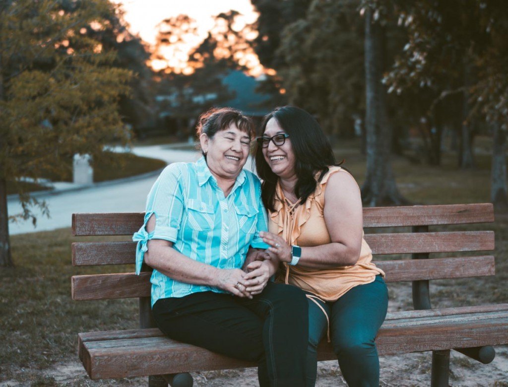 two women laughing on a park bench