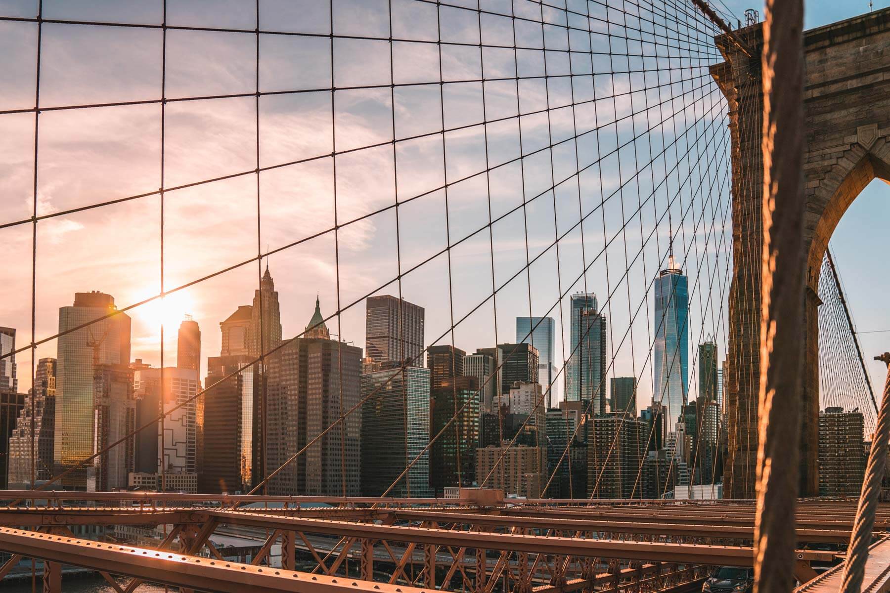 the new york skyline through the lines of the bridge during sunset