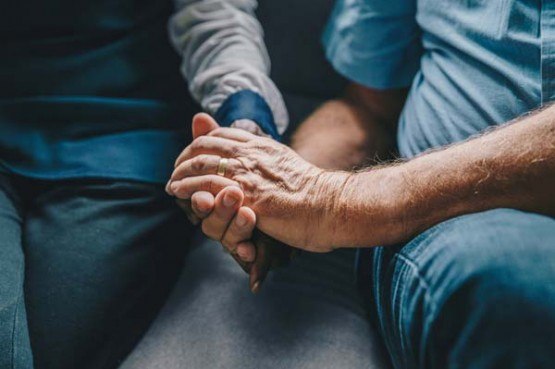 a young man softly holding an elder man's hand for comfort