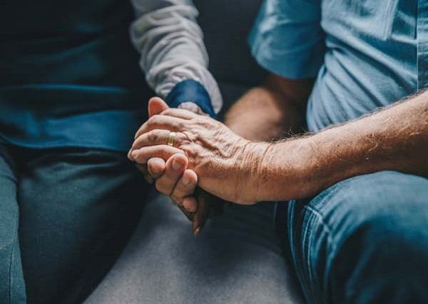 a young man softly holding an elder man's hand for comfort