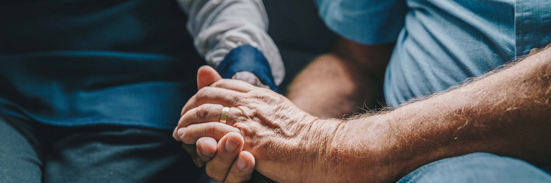 a young man softly holding an elder man's hand for comfort